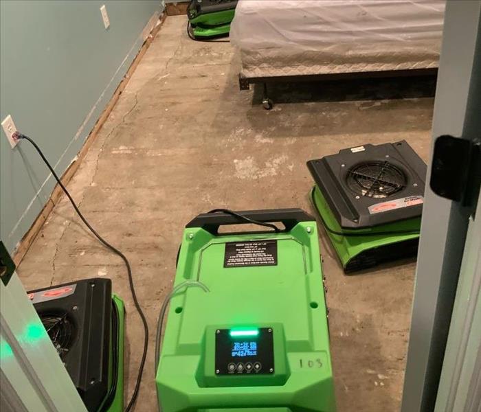 green air mover and dehumidifier on plywood sub floor by the bed